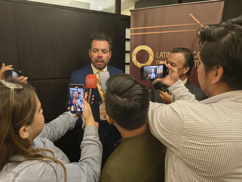 Periodistas entrevistan a un ejecutivo frente al banner de LAQI